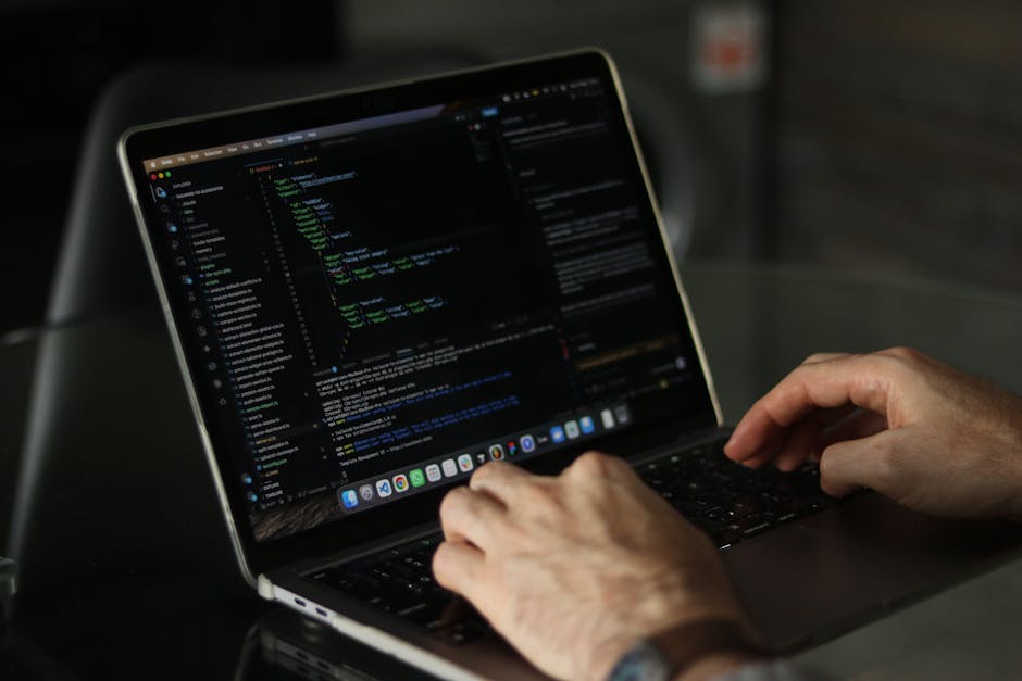 A close-up view of a laptop computer displaying lines of programming code in a dark-themed editor, placed on a wooden desk. To the right of the laptop, there is a ceramic coffee mug with a printed mes